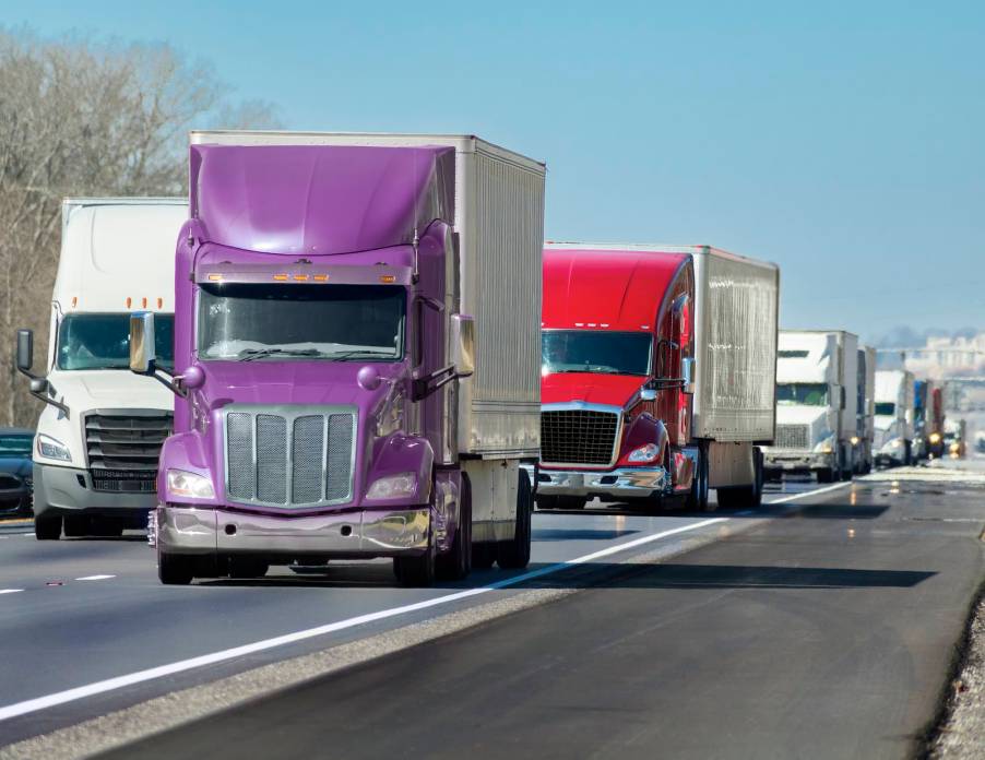 Purple semi-truck at the head of a convoy on the highway