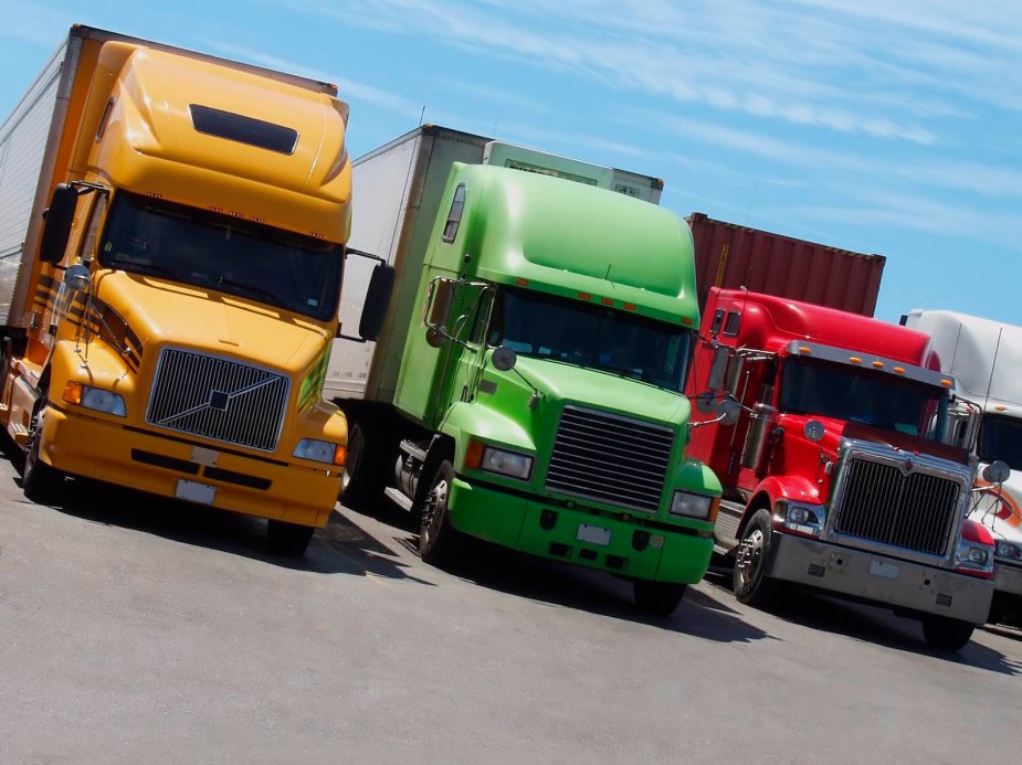 Orange, green, and red semi trucks parked in a lot for a truck show.