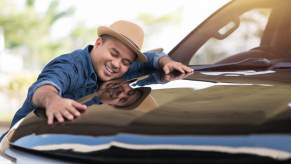 A car shopper smiles and hugs his car after finding it and gaining ownership.