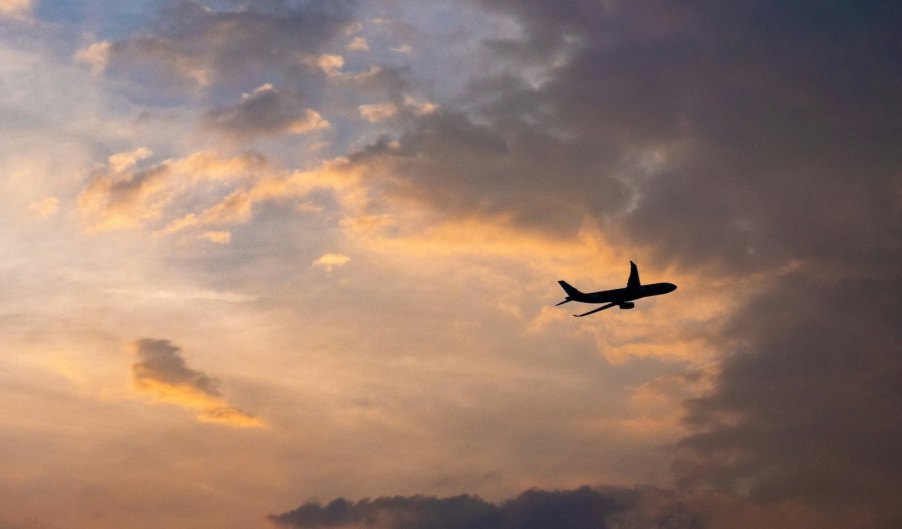 The silhouette of a jet airplane flying across a sunset.