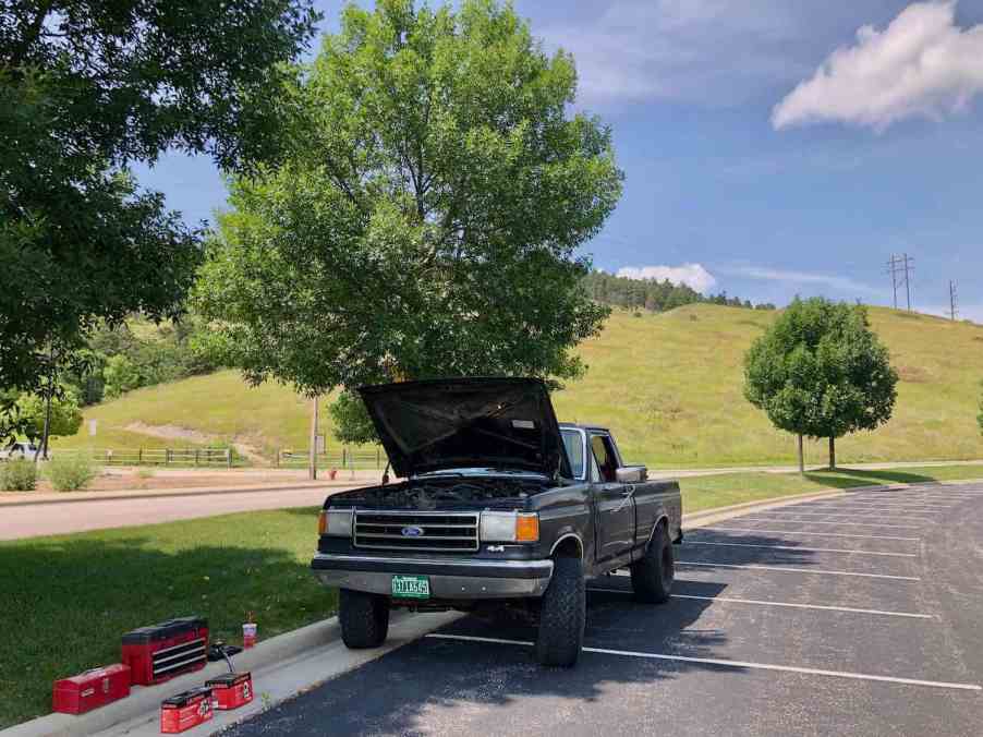 Black Ford F-150 pickup truck in a parking lot with its hood up for maintenance.