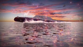 A Migaloo submarine yacht breaching in front of the ocean.