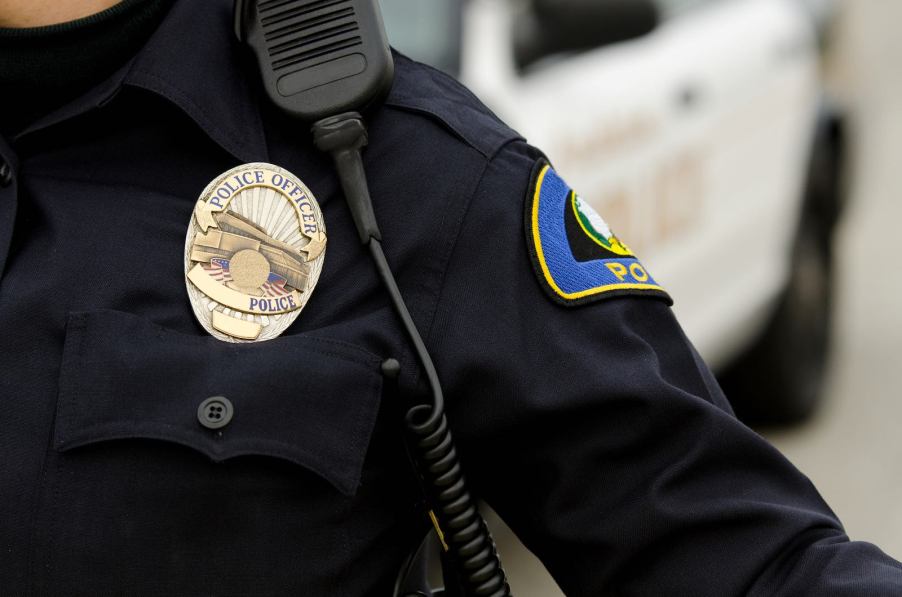 A police officer in uniform wearing a badge and radio.