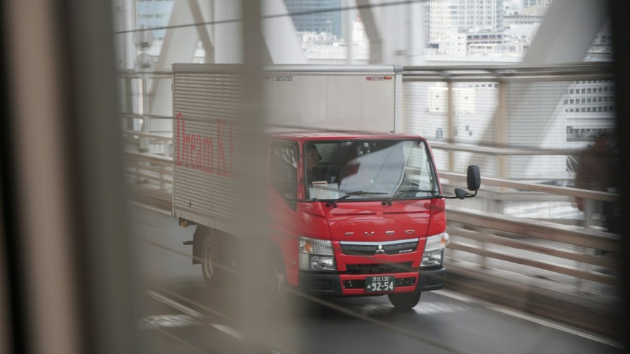 Red cargo truck with a white box crosses a bridge on a highway