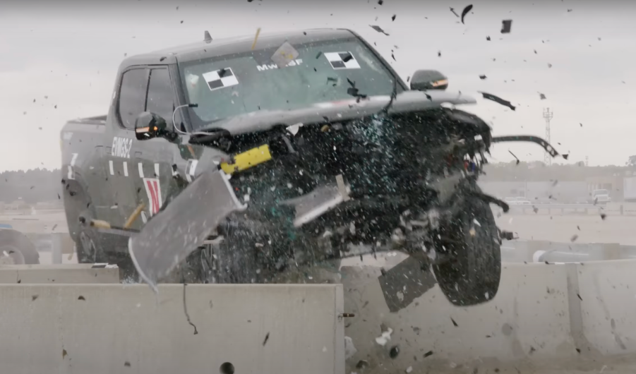 Green Rivian R1T electric pickup truck smashes through a guard rail barrier