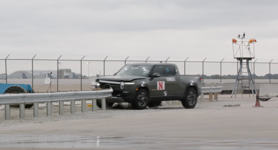 Green Rivian truck destroying a guard rail in a safety test.