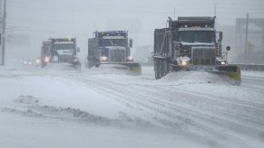 A row of three snowplow trucks clearing a road after a storm.