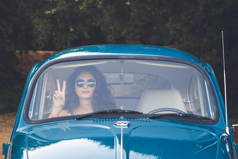 Woman sits in the passenger seat of an old Volkswagen Beetle.