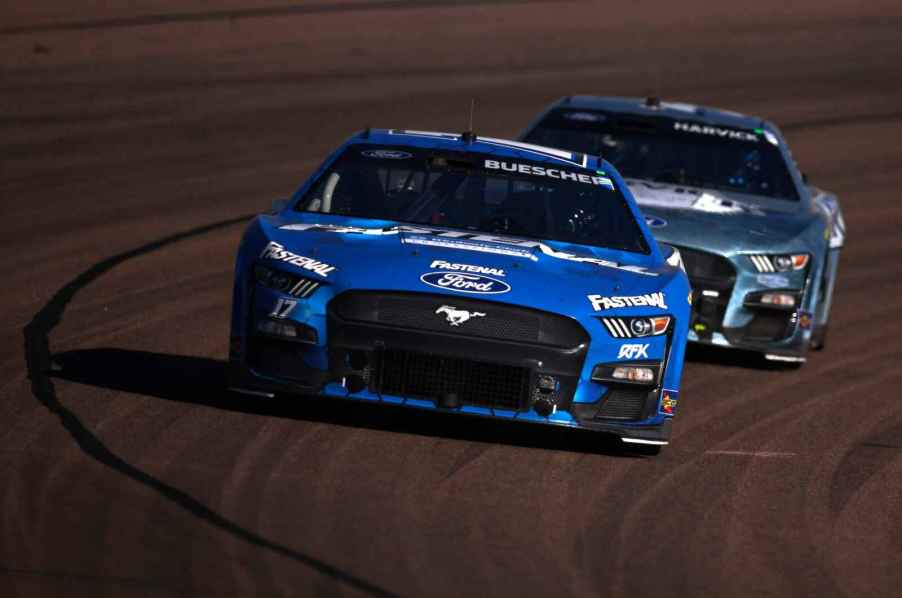 A blue Ford Mustang NASCAR car races in front of a another blue Ford NASCAR car