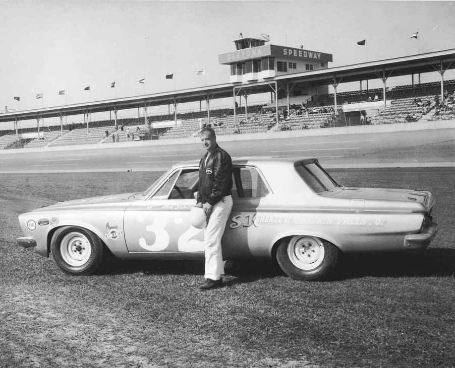 A photo of Bob James at the NASCAR Daytona 500 standing next to a stock 1963 Plymouth.