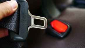 A hand is shown holding up the male end of a car seat belt buckle with red plastic male end in background