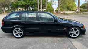 Silhouette of a black BMW wagon parked in front of trees