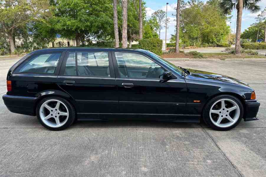 Silhouette of a black BMW wagon parked in front of trees