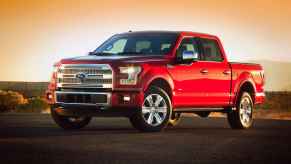 A 2015 Ford F-150 pickup truck parked in left front angle view front wheels turned in headlight glimmering sun setting behind parked on smooth black pavement