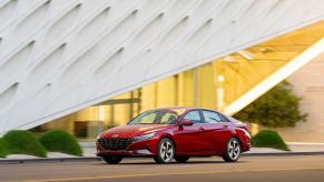 A 2021 Hyundai Elantra cruises by an modern structure.