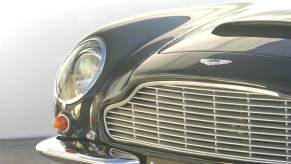 A closeup shot reveals an Aston Martin DB6, a GT car owned by Mick Jagger, Paul McCartney, and King Charles III.