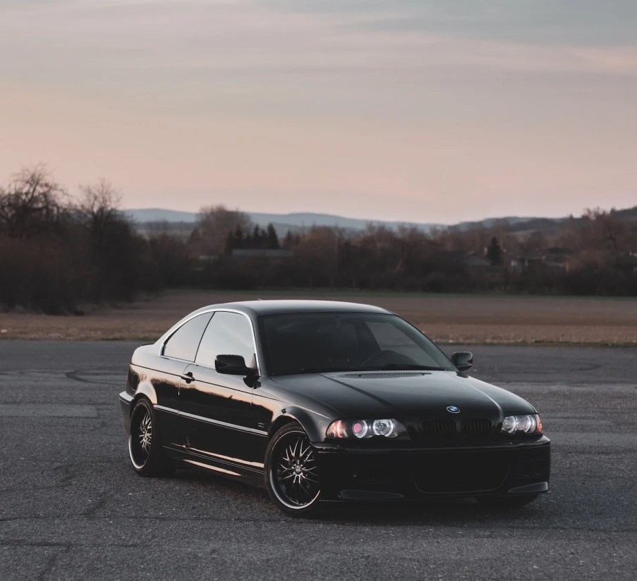 Black BMW 3 Series parked on pavement, trees visible in the background.