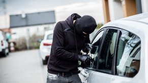 Man in a mask breaks into a silver car.