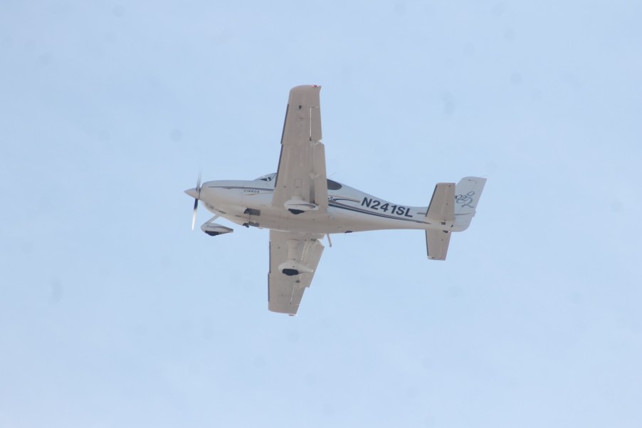 Underside of an ultralight white aircraft against a blue sky.