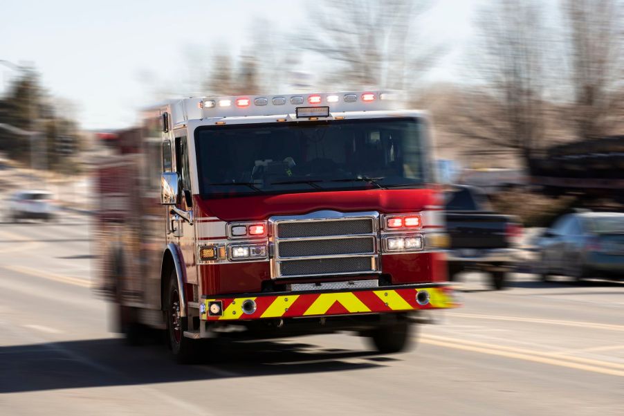 Red fire truck races down a suburban street to a house fire.