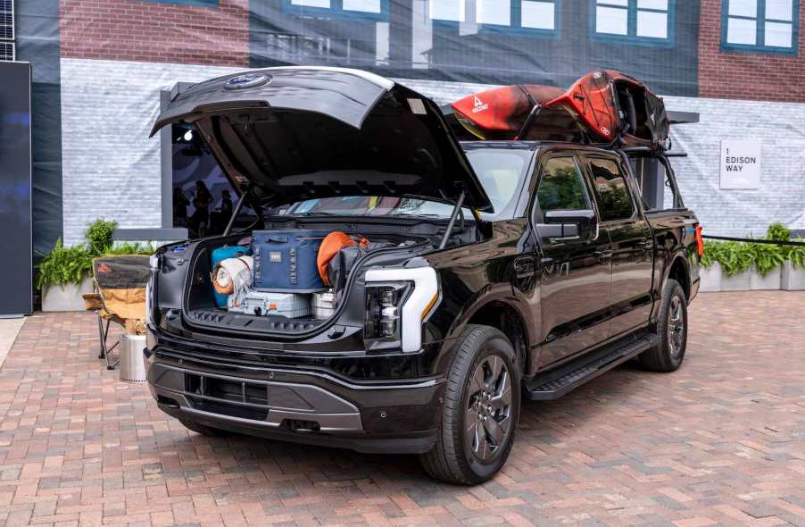 An electric Ford Lightning pickup truck filled with camping gear, with an open frunk.