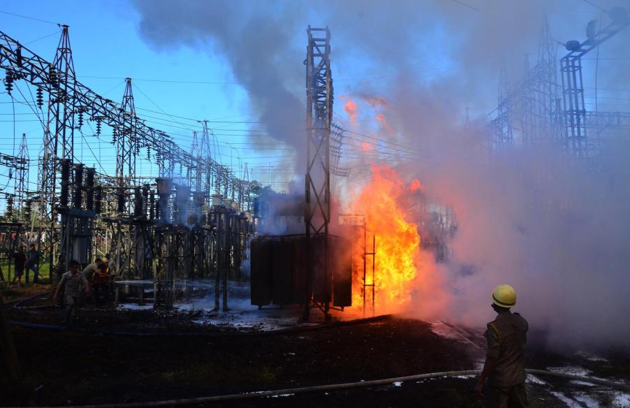 Huge orange flames engulfing a power transformer in a yard of power lines