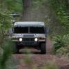 A Humvee in the woods drives with its lights on.