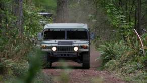 A Humvee in the woods drives with its lights on.