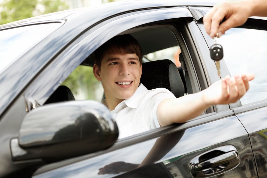 Teenage boy sitting in a car driver's seat gets handed the keys.