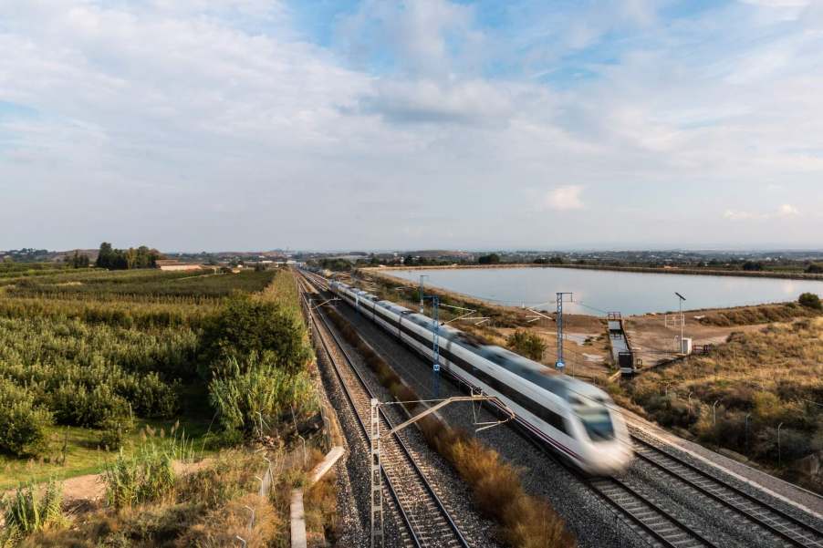 High speed rail train in the countryside, a lake visible behind the tracks.