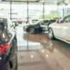 A blurry daylight shot of inside of dealership showroom several cars parked in view