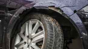 A car crash is shown in very close view dark colored car with damaged right front end is shown crooked wheel cracked fender