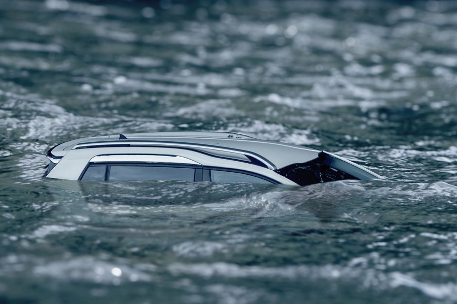 A silver SUV is almost fully submerged in water in right profile view