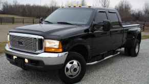 A black diesel pickup truck with dual rear wheels parked on gravel in left front angle view