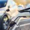 A white EV charger shown plugged into frame right while a blurred out car is parked with a charger plugged in the background