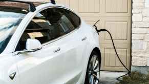 A white EV parked in front of a beige garage door at a residential home plugged into home EV charger