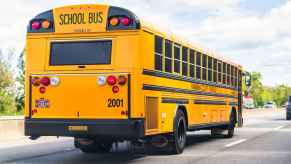 A yellow school bus driving on a paved road traffic in background full right rear angle view