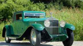 Kelly Green 1929 Rolls Royce coupe parked in front of trees.