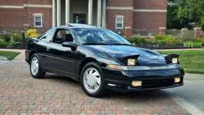 A black 1990 Mitsubishi Eclipse parked at right front angle view on brick path museum of art in background