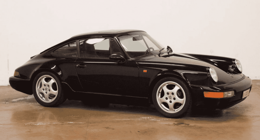 A black 1991 Porsche 911 964 is parked inside a garage floor with white walls in right profile view