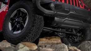 The right front underside corner of a red 2020 Jeep Wrangler Rubicon climbing rocks in close view