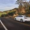 A white 2024 Subaru Legacy drives on a winding hilly road away from the viewer in left rear angle