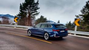 A BMW station wagon races along a mountain road, trees visible in the background.