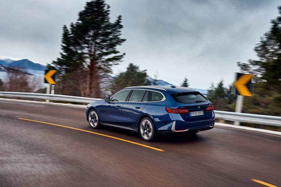 A BMW station wagon races along a mountain road, trees visible in the background.