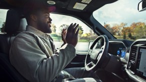 A man sits in a Ford F-150 truck with both hands held above the steering wheel while hand-free driver assistance tech BlueCruise is engaged