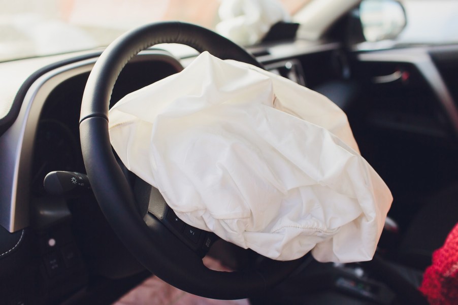 A white crumpled airbag sticking out of a steering wheel center.