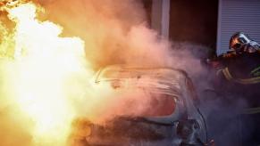 Firefighter puts out a burning car, with a hose.