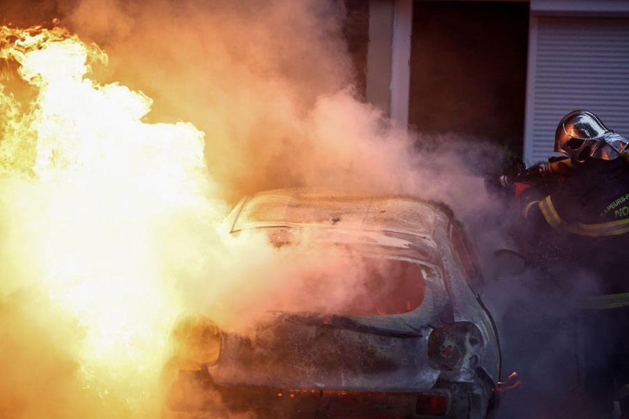 Firefighter puts out a burning car, with a hose.