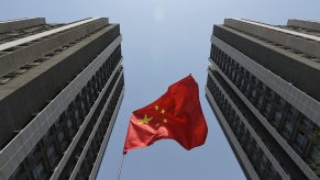 A red Chinese flag between two skyscrapers.