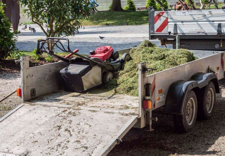 A lawn mower sits on a professional lawn service's trailer with clippings.